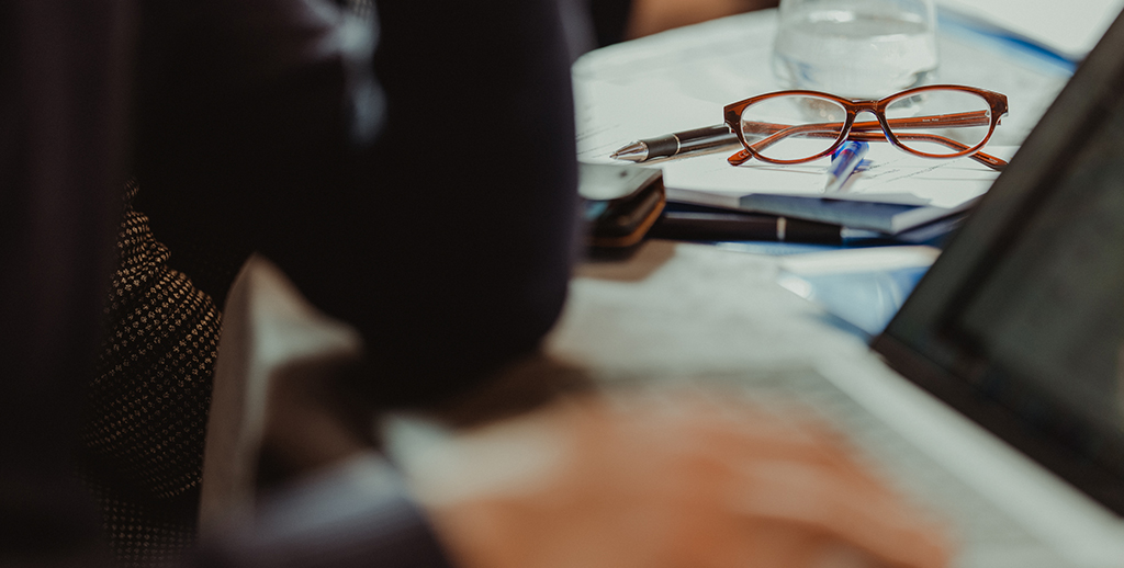 Lady working at desk with glasses in background